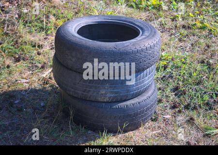 Vieux pneus de voiture pliés dans une pile reposent sur l'herbe. Banque D'Images