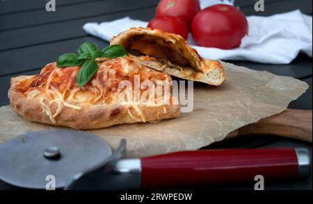 Pizza calzone découpée avec sauce tomate, pesto vert et fromage sur assiette en bois Banque D'Images