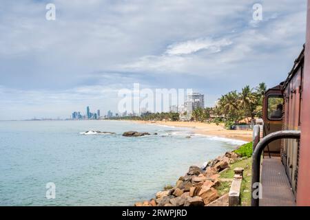 Train arrivant à Colombo avec plage en arrière-plan et horizon de la ville. Transport ferroviaire. Asie, Sri Lanka, Colombo Banque D'Images