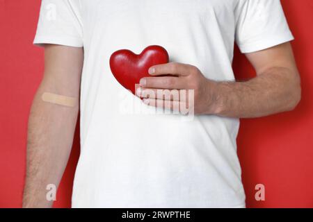 Concept de don de sang. Homme avec le plâtre adhésif sur le bras tenant le coeur rouge sur fond de couleur, closeup Banque D'Images