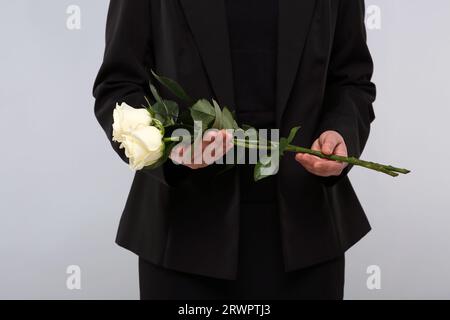 Femme avec des fleurs roses blanches sur fond gris clair, gros plan. Cérémonie funéraire Banque D'Images