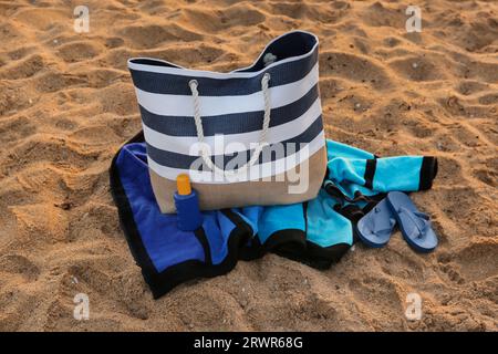 Sac de plage élégant, tongs, crème solaire et serviette sur le sable Banque D'Images