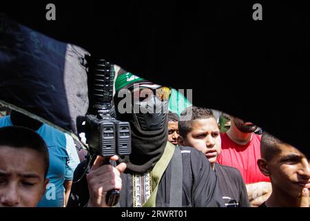Un tireur masqué prend part aux funérailles de Mahmoud al-Sadi, 23 ans, Mahmoud Ararawi, 24 ans, et ATA Yasser Musa, 29 ans, drapés dans le drapeau du Hamas et du Jihad islamique lors de leurs funérailles dans le camp de réfugiés de Djénine, en Cisjordanie. Les responsables palestiniens de la santé disent que le nombre de morts au cours d'une journée de combats entre Israël et les Palestiniens en Cisjordanie occupée et dans la bande de Gaza est passé à six, dont quatre à Djénine. L'armée a déclaré que les forces ont effectué une frappe rare mardi avec un drone suicide pendant l'opération et ont échangé des tirs avec des hommes armés à Djénine. Banque D'Images