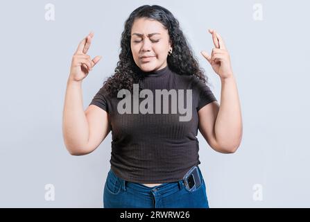 Fille latine croisant les doigts faisant un vœu. Jeune femme souriante faisant un vœu avec un geste plein d'espoir Banque D'Images