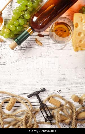 Bouteille de vin blanc, raisin, miel, fromage, verre à vin avec tire-bouchon, bouchons et corde sur planche de bois blanche. Vue de dessus avec espace de copie. Banque D'Images