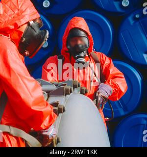 2 hommes remplissant un conteneur de produits chimiques dans des combinaisons de protection rouges avec des masques respiratoires. Numérique et diapositive 6x6 Banque D'Images