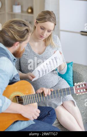 homme jouant de la guitare aux côtés de sa femme enceinte Banque D'Images
