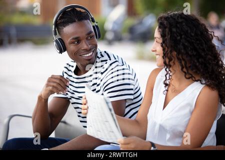 couple multiracial assis sur un banc l'homme porte des écouteurs Banque D'Images