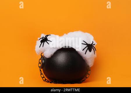 Joyeux concept de vacances Halloween. Chaudron de sorcière avec des araignées noires sur fond orange, espace de copie. Chaudron de sorcière comme socle pour les produits Banque D'Images