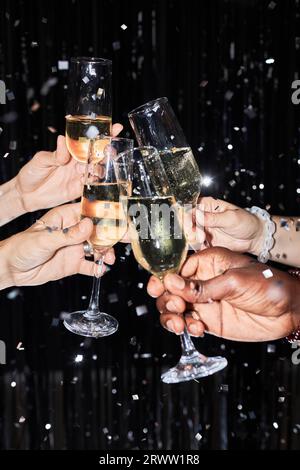 Gros plan d'un groupe d'amis grillant avec des verres à champagne à la fête sur fond scintillant avec des confettis Banque D'Images