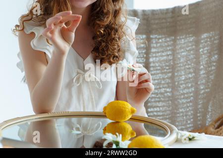 Fille, vêtue de blanc, tient une fleur de camomille dans sa main, au-dessus d'un miroir avec des fruits. Composition estivale. Partie du corps. Focus sur la camomille Banque D'Images