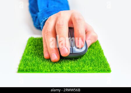 Vue rapprochée d'une main à l'aide d'une souris d'ordinateur fixée sur un tapis de souris en herbe. Banque D'Images