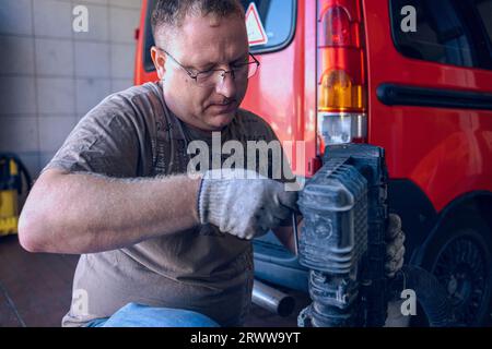 Un homme avec des lunettes entretient une voiture dans un garage. Réparation de voiture par un spécialiste expérimenté dans un atelier de réparation de voiture. Remplacement de l'huile et du filtre dans la voiture. Banque D'Images