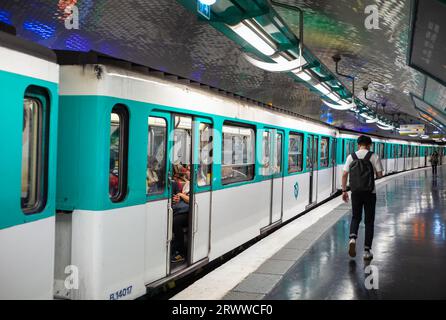 Un homme marche sur le quai alors qu'un train du métro parisien se prépare à sortir de la station Gambetta sur la ligne 4 à Paris, en France. Banque D'Images