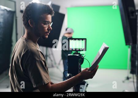 Jeune caméraman professionnel lisant le script avant de tourner en studio Banque D'Images