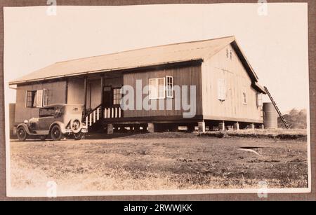 Une des images d'une série d'images de la résidence secondaire des Bungeys à Kapsabet au début des années 1930 Cette image montre l'avant de la maison avec une voiture garée à l'extérieur. Un couple européen et leur fils sont dans le jardin, le garçon joue avec un chien. Légende de la page originale : vues de la maison et du jardin Kapsabet. Banque D'Images