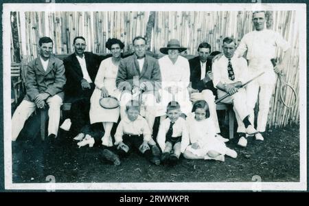 Photographie de groupe d'Européens lors d'une fête de tennis. Six hommes, deux femmes et trois enfants sont assis devant une clôture en bambou, avec Charles Bungey au centre du groupe. La plupart portent des blancs de tennis et certains portent des raquettes. Légende originale du manuscrit : « une partie de tennis ». Banque D'Images