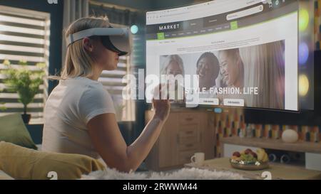 Femme dans le casque VR choisit des vêtements dans le magasin en ligne refroidissant à la maison. Hologramme futuriste 3D montre des widgets dans le menu utilisateur et l'interface du site Web du magasin de vêtements. Animation VFX. Concept de shopping en ligne. Banque D'Images