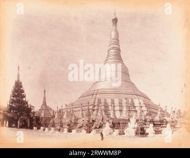 Vue de Shwedagon Zedi Daw connue sous le nom de Grande Pagode Dragon ou Pagode d'Or à Rangoon. Le stupa doré géant est entouré de stupas votifs plus petits subsistants. Une plus grande entrée de pagode peut être vue à gauche. Une figure birmane locale se tient devant le stupa dans le complexe du temple. Légende manuscrite : She Dagon Pagoda Rangoon. Banque D'Images