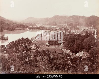 Vue de Lady Horton's Walk donnant sur le lac Kandy et Sri Dalada Maligawa, le temple bouddhiste de la relique de la dent sacrée. Un stupa blanc peut être vu dans le complexe du temple. Il y a des collines en arrière-plan et un feuillage luxuriant avec des palmiers entourant la scène. Inscrit sur le négatif : [Kandy] de Lady Horton's Walk 962-Scowen & Co. Légende : Kandy. Banque D'Images