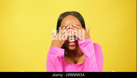 Belle jeune femme couvre les yeux, riant, souriant, fond de studio jaune Banque D'Images