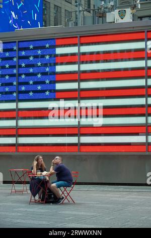 Un couple de touristes s'arrête pour un repos et une collation à Times Square devant le drapeau américain géant au bureau de recrutement de l'armée américaine. Été 2023. Banque D'Images