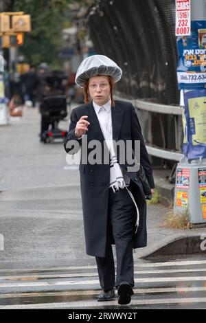 Un jeune homme juif marche sur Lee Avenue pendant une pluie légère portant un chapeau de pluie fait maison. À Williamsburg, Brooklyn, New York. Banque D'Images