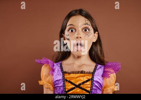 Expression du visage, fille choquée en costume d'Halloween regardant la caméra sur fond brun, effrayante Banque D'Images