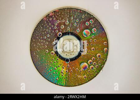 CD sur fond blanc avec des gouttes d'eau arc-en-ciel sur la surface métallique réfléchissante Banque D'Images