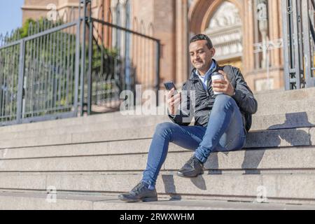 Jeune homme latino assis sur quelques escaliers avec espace de copie. Banque D'Images