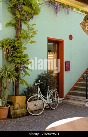 Un vélo solitaire debout près du mur coloré entouré de plantes vertes et méditerranéennes à Caorle, en Italie Banque D'Images