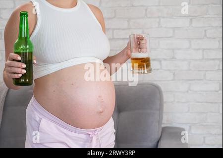 Femme enceinte tenant verre et bouteille de bière. Banque D'Images