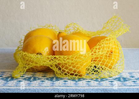 Citrons frais jaunes dans un sac en filet en plastique sur une nappe bleue Banque D'Images