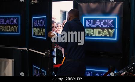 Foule de clients divers à l'entrée poussant pour ouvrir la porte d'entrée, devenant fou le Black friday. Les clients se disputent avec un agent de sécurité afro-américain qui font la queue. Chasse aux bonnes affaires. Banque D'Images