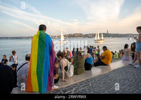 Lisbonne, Portugal. 17 juin 2023 Homme avec drapeau arc-en-ciel gay défilé à promenade. Homme gay debout à l'extérieur pendant le mois de la fierté. Communauté LGBT portant un drapeau arc-en-ciel regardant un yacht sur l'eau Banque D'Images