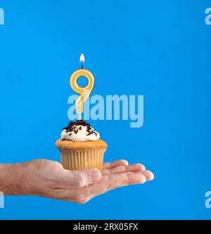 Main livrant cupcake d'anniversaire - bougie numéro 9 sur fond bleu Banque D'Images