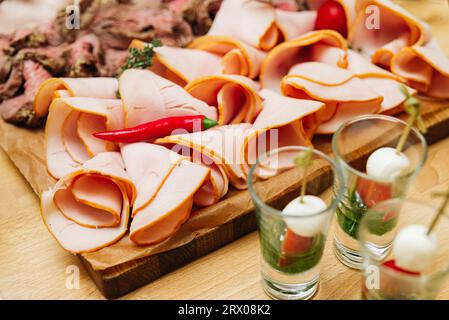 Tranches de jambon fumé sur une planche de bois. Fines tranches de charcuterie et de canapés caprese en doses. Gros plan. Banque D'Images