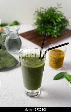 Smoothie vert sain avec des herbes et des fruits de la passion sur fond blanc. Un verre de smoothie vert à côté de quelques fruits et légumes, et une cruche à eau Banque D'Images