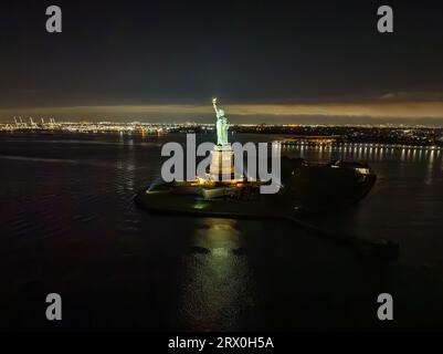 Une vue aérienne de la Statue de la liberté la nuit avec les lumières du New Jersey en arrière-plan Banque D'Images