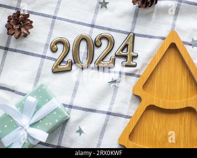 Plaque en bois de forme d'arbre de noël vide avec 2024 sur fond de serviette. Assiette en bois du nouvel an parmi les cônes d'un sapin, étoiles décoratives et cadeau Banque D'Images