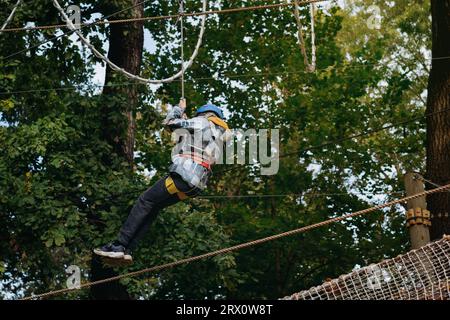 adolescent descendant en tyrolienne dans le parc d'aventure en passant le parcours d'obstacles. parc à cordes élevées à l'extérieur Banque D'Images