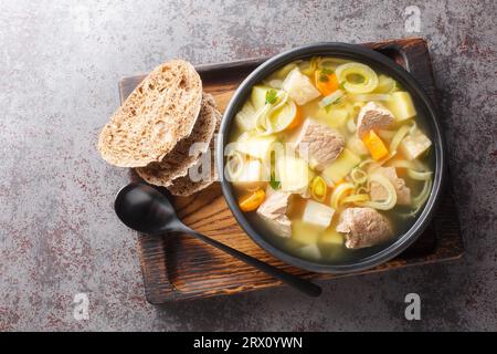 Soupe Kottsoppa avec viande bouillie, carottes hachées, oignons, panais, céleri et poireaux gros plan sur une assiette sur la table. Vue de dessus horizontale Banque D'Images