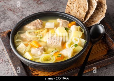 Soupe Kottsoppa avec viande bouillie, carottes hachées, oignons, panais, céleri et poireaux gros plan sur une assiette sur la table. Horizontal Banque D'Images