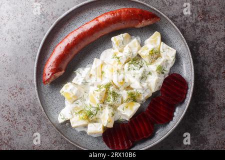Saucisse fumée avec pommes de terre dans la sauce à la crème avec l'aneth et les betteraves bouillies gros plan sur une assiette sur la table. Vue de dessus horizontale Banque D'Images