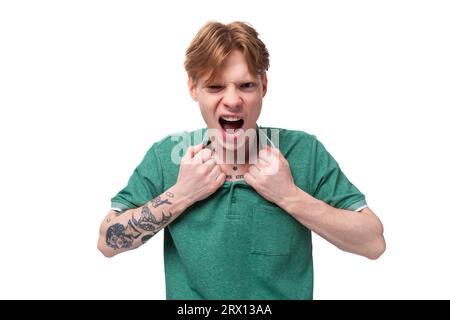 Un jeune homme gingembre brillant avec un tatouage sur le bras, vêtu d'un T-shirt vert à manches courtes, crie de colère Banque D'Images