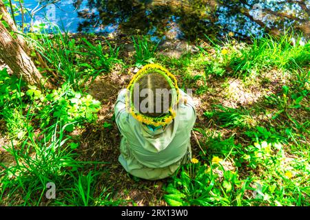 fille au printemps. Enfant sur le fond de l'herbe de printemps. La fille dans une couronne de pissenlits jaunes assis sur l'herbe verte. Vue d'en haut. Ressort Banque D'Images