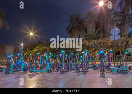 Vue imprenable sur le parking de la ville pour scooters électriques la nuit à Malaga. Gros plan d'un grand nombre de scooters électriques garés pleins de couleurs et de variété. Banque D'Images