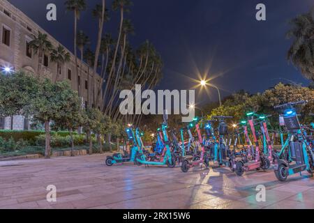 Vue imprenable sur le parking de la ville pour scooters électriques la nuit à Malaga. Gros plan d'un grand nombre de scooters électriques garés pleins de couleurs et de variété. Banque D'Images