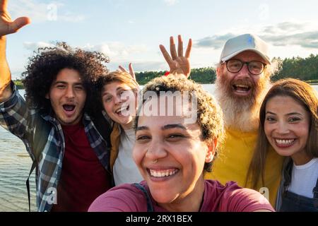 Jeune groupe multiracial de gens à la mode s'amusant ensemble en vacances - divers amis millénaires prenant le portrait de selfie ensemble tout en profitant du temps libre sur une plage de lac de forêt - concept d'amitié. Photo de haute qualité Banque D'Images