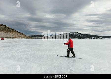 Homme en manteau rouge sur lac gelé ski de fond en montagne Banque D'Images